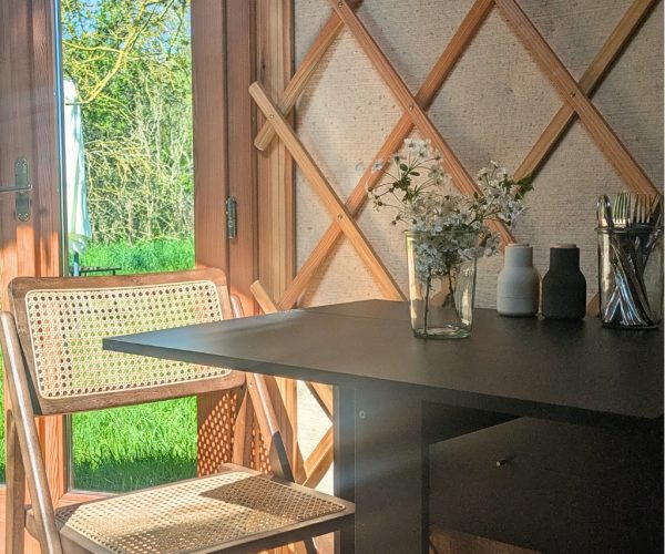 Essbereich mit Geflechtstuhl und Naturblick durch offene Tür in der Jurte Seenplatte